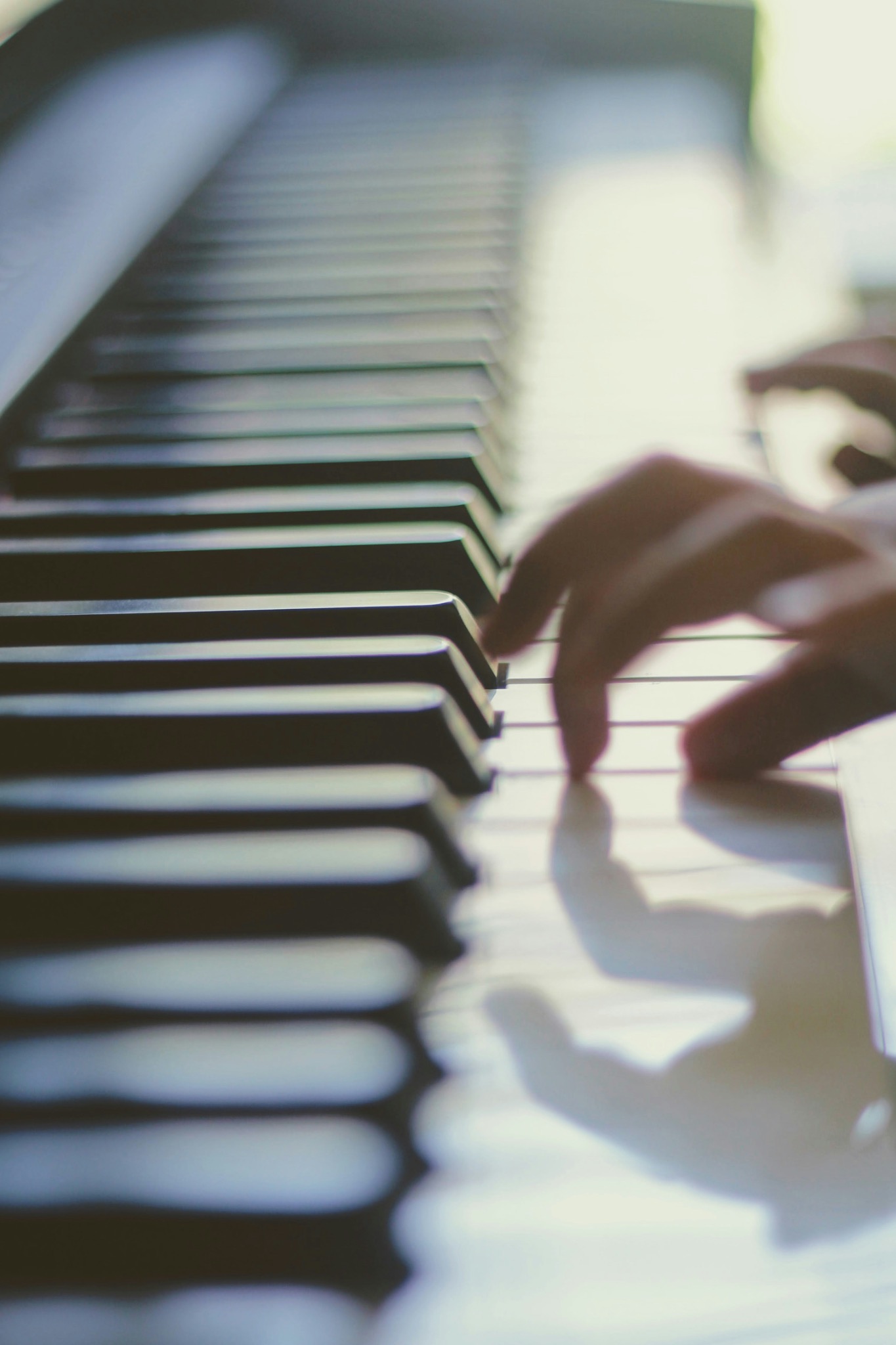 Hands playing piano keys in soft light